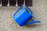 Blaue Gießkanne hängt an heller Gartenwand